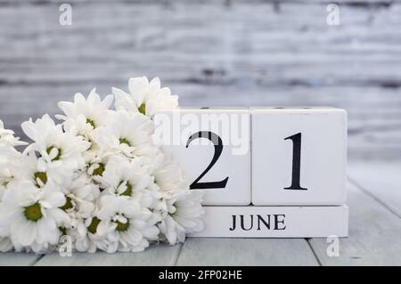 Sommersonnenwende Kalendarblöcke aus weißem Holz mit dem Datum des 21. Juni und weißen Gänseblümchen. Selektiver Fokus mit unscharfem Hintergrund. Stockfoto