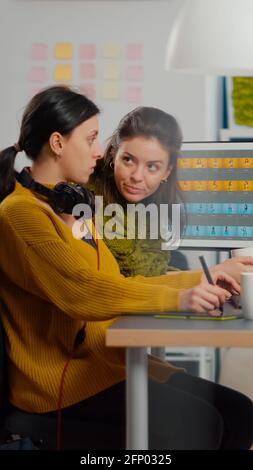 Selbstbewusste Frauen Foto-Editoren sitzen am Arbeitsplatz in kreativen Studio Retusche Foto, Art Director erklärt Farbe greding Technik. Retuschers Bearbeitung mit Zeichentablett und Stylus Bleistift Stockfoto