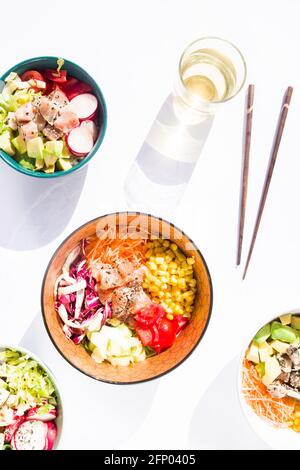 Verschiedene Poke Schüsseln mit Gemüse und Lachs o, Thunfisch, edamame Bohnen, auf einem weißen Hintergrund mit Essstäbchen und einem Glas weißem Whine, Draufsicht , Stockfoto