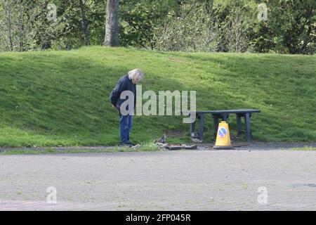 Der Mann schaut auf die Stelle, an der der Wurfbehälter durch Feuer zerstört wurde Durch Vandalen mit Verkehrskegel, die Personen vor dem warnen Gefahr Stockfoto