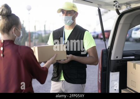 Porträt der Geburt Mann trägt Gesichtsschutzmaske für Coronavirus Ausbreitung Prävention. Frau Hand nimmt eine Lieferung von Boxen von deliveryman. Stockfoto