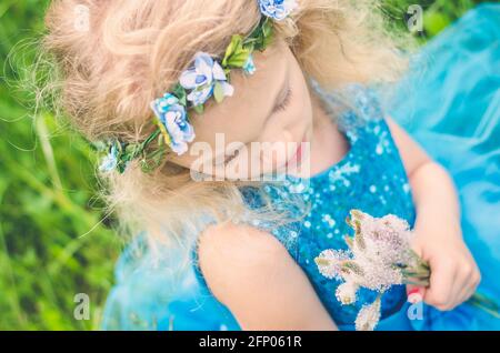 Schöne blonde Mädchen sitzt im Gras hält Haufen von Wiesenblumen Stockfoto