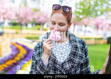 Junge Frau, die im öffentlichen Park Kirschblüte riecht Stockfoto