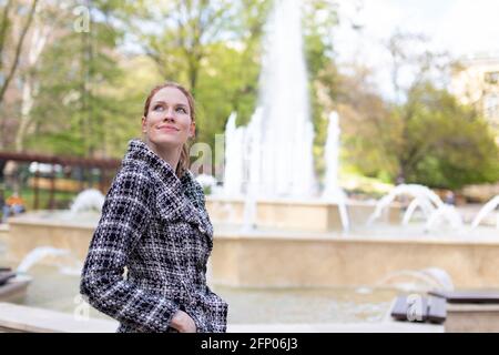 Junge Frau, die beim Spaziergang im Park am Brunnen den Himmel beobachtete, kalter Frühling Stockfoto