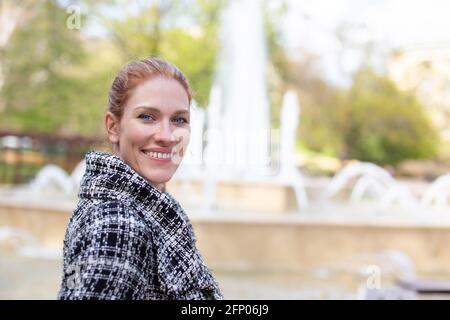 Junge kaukasische Frau, die während des Frühlings in die Kamera schaut, waagerecht auf den Brunnen Stockfoto