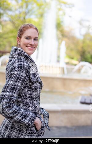 Junge kaukasische Frau, die während des Frühlings in die Kamera schaut, um den Brunnen zu betrachten Stockfoto