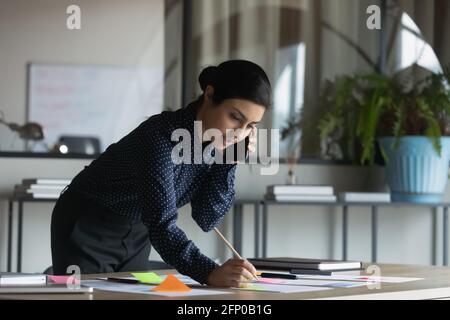Junge indische Angestellte sprechen mit Papierkram über das Handy Stockfoto