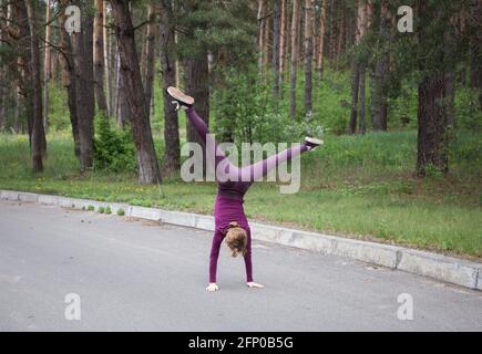 Junge unkenntlich schlanke Mädchen in Sportswear steht auf dem Kopf tun einen akrobatischen Coup. Gymnastik-Übungen. Aktivität, Heiterkeit, Gleichgewicht. Heilen Stockfoto