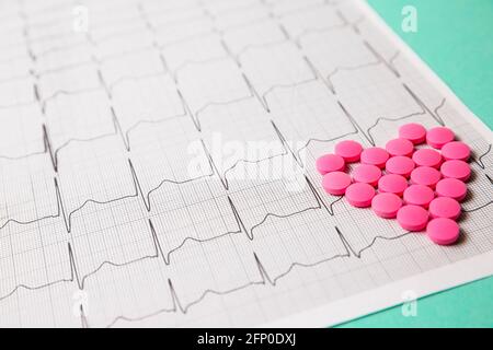 Ein Haufen roter Pillen in Herzform auf dem Kardiogramm. Medizinisches Konzept. Stockfoto