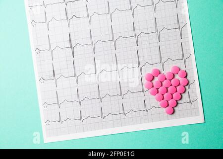 Ein Haufen roter Pillen in Herzform auf dem Kardiogramm. Medizinisches Konzept. Stockfoto