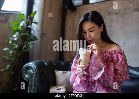 Hübsche junge asiatische Frau trinkt Eiskaffee in einem modernen Café. Stockfoto