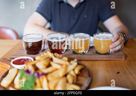 Mann probiert verschiedene saisonale Craft Beer im Pub. Bierprobenehmer in kleinen Gläsern, einzeln in Löchern in einem einzigartigen Holztablett platziert Stockfoto