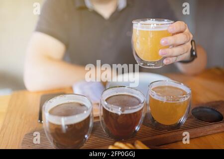 Mann probiert verschiedene saisonale Craft Beer im Pub. Bierprobenehmer in kleinen Gläsern, einzeln in Löchern in einem einzigartigen Holztablett platziert Stockfoto