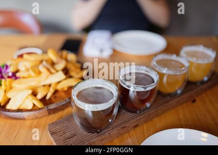 Mann probiert verschiedene saisonale Craft Beer im Pub. Bierprobenehmer in kleinen Gläsern, einzeln in Löchern in einem einzigartigen Holztablett platziert Stockfoto