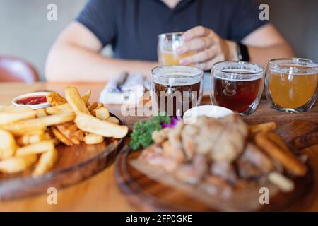 Mann probiert verschiedene saisonale Craft Beer im Pub. Bierprobenehmer in kleinen Gläsern, einzeln in Löchern in einem einzigartigen Holztablett platziert Stockfoto