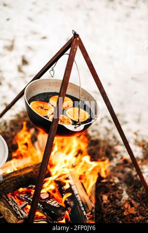 Von oben traditionellen Glühwein mit Scheiben von Orange Vorbereitung Im Topf über brennenden Baumstämmen im Winter auf dem Land Stockfoto