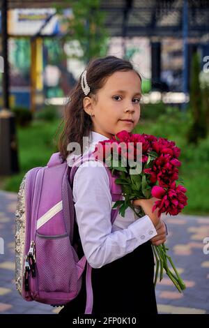 Kleines schönes Schulmädchen in einem weißen Hemd mit Blumen Stockfoto