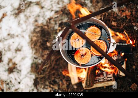 Von oben traditionellen Glühwein mit Scheiben von Orange Vorbereitung Im Topf über brennenden Baumstämmen im Winter auf dem Land Stockfoto