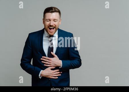 Aufgeregter Geschäftsmann im Anzug, der die Arme auf dem Bauch hält und hat Spaß Stockfoto