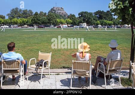 Die Menschen beobachten Cricket-Spiel in historischen Liston Cricket Ground Landschaft Teil des Spianada Square Greek Corfu Town mit Old Fortress Beyond Greece EU Stockfoto