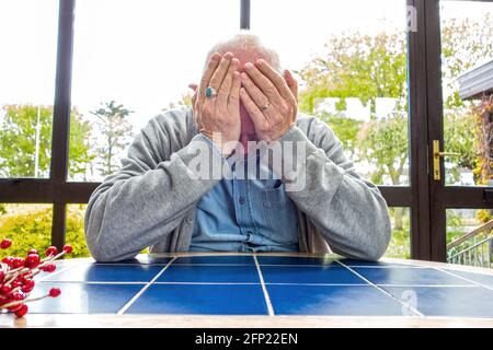 Ein Mann saß an einem Tisch, hielt seinen Kopf in den Händen, beunruhigt, deprimiert, bestürzt Stockfoto