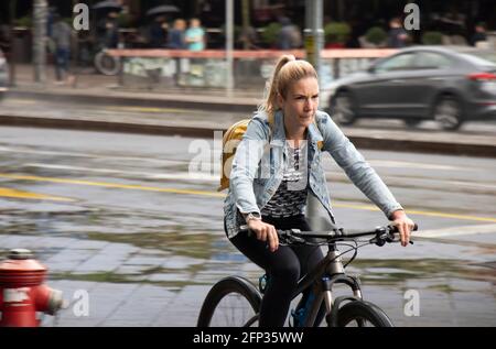 Belgrad, Serbien - 13. Mai 2021: Eine junge blonde Frau, die an einem regnerischen Tag auf einem Bürgersteig in der Stadt Fahrrad fährt Stockfoto