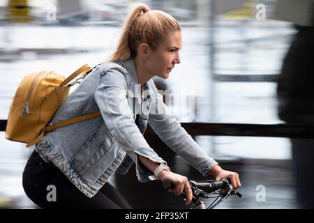 Belgrad, Serbien - 13. Mai 2021: Eine junge blonde Frau, die an einem regnerischen Tag auf einer Stadtstraße Fahrrad fährt Stockfoto