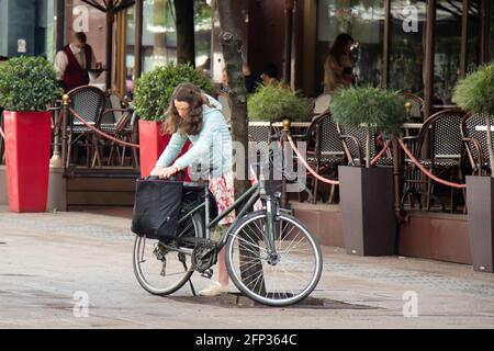 Belgrad, Serbien - 13. Mai 2021: Eine junge Frau packte doppelte Fahrradtaschen auf ihrem geparkten Fahrrad auf einer Straße in der Nähe der Cafeterrasse Stockfoto