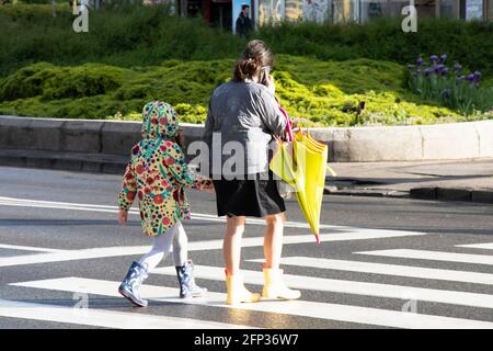 Belgrad, Serbien - 13. Mai 2021: Frau und ein Mädchen gehen Hand in Hand, während sie an einem sonnigen und regnerischen Tag die Straße überqueren Stockfoto