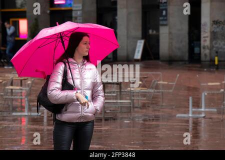Belgrad, Serbien - 13. Mai 2021: Eine junge Frau, die allein unter dem Schirm steht und an einem regnerischen Tag auf dem Stadtplatz wartet Stockfoto