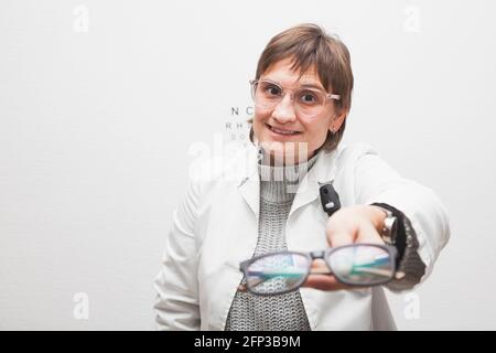 Der Mitarbeiter eines Optikers gibt einem Kunden eine neue Brille, die er in der ersten Person sieht. Die Brille ist unscharf und das Gesicht des Optometristen ist fokussiert. Stockfoto