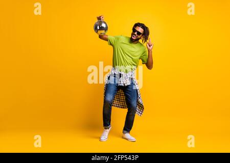 In voller Länge Foto von jungen verrückten Mann tanzen genießen Musik Party halten Glitter Ball tragen Jeans isoliert über gelbe Farbe Hintergrund Stockfoto