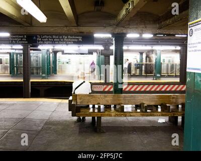 Ein einsitzender Mann sitzt auf einer Holzbank und wartet darauf Ein U-Bahn-Zug auf einem Bahnsteig in New York City Stockfoto