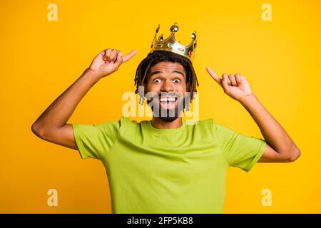Foto von schönen afro Mann glücklich Lächeln aufgeregt Show Point Index Finger Krone tragen grüne T-Shirt isoliert über gelbe Farbe Hintergrund Stockfoto