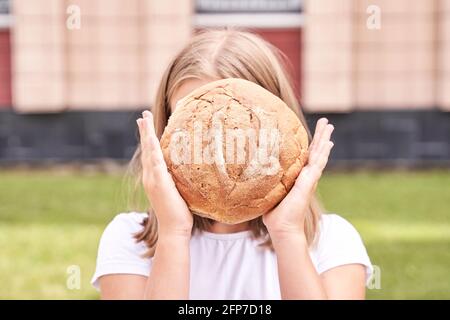 Das Kind hält ein rundes Brot. Gesunde Ernährung. Großes frisches Bäckerbrötchen tragen Stockfoto