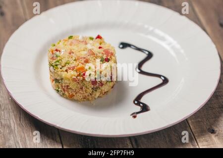 Nahaufnahme eines Tellers Tabbouleh-Salat mit Gemüse Und knabberte auf einer hölzernen Oberfläche Stockfoto