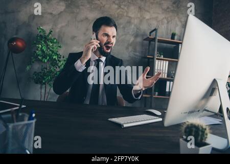 Foto eines ärgerlichen, aggressiven bärtigen Mannes, der auf dem Schreibtisch sitzt und telefonieren kann Look Bildschirm pc tragen Anzug Hemd Krawatte im modernen Büro In Innenräumen Stockfoto