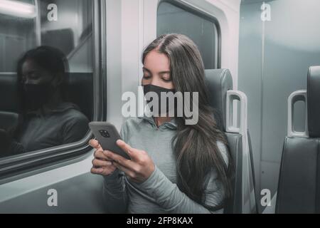 Öffentliche Verkehrsmittel pendeln Frau Pendler in der Nacht trägt Gesichtsmaske Reiten U-Bahn mit Handy. Asiatischer Passagier mit Gesichtskoronavirus, der sich überdeckt Stockfoto