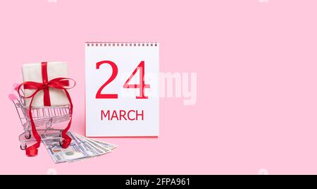 Tag des 24. märz. Eine Geschenkbox in einem Einkaufswagen, Dollars und ein Kalender mit dem Datum des 24. märz auf einem rosa Hintergrund. Frühlingsmonat, Tag des y Stockfoto