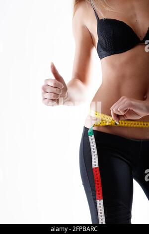 Eine schlanke junge Frau, die ihre Hüften misst, gibt einen Daumen nach oben für ein Konzept zur Gewichtsreduktion, Diät, Bewegung und einem gesunden Lebensstil Stockfoto