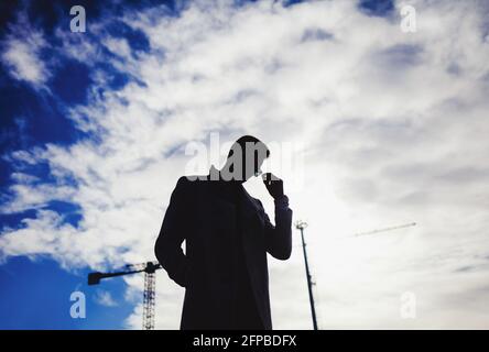 Silhouettierter Mann in Sonnenbrille, der auf blauem Himmel Hintergrund steht Stockfoto