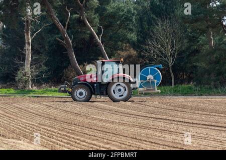 Woodbridge, Suffolk, Großbritannien April 24 2021: Ein Traktor, der Bewässerungsausrüstung trägt, die bereit ist, Wasserleitungen zur Bewässerung eines landwirtschaftlichen Feldes abzulegen Stockfoto