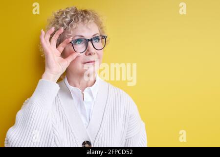 Reife Frau mit ernster und konzentrierter selbstbewusster Optik, Brainstorming und Gedanken an herausfordernde Probleme, posiert isoliert auf Gelb, trägt el Stockfoto