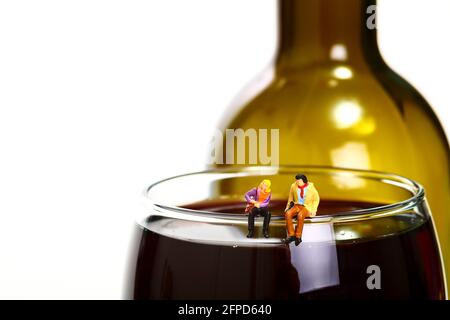 Miniaturfigur Mann und Frau saßen auf einem Glas Rotwein mit einer Weinflasche im Hintergrund Stockfoto
