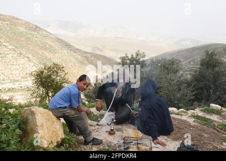 Beduin oder arabischer Nomade sitzt mit seinen Söhnen, einer von ihnen lächelt, er atmet aus, während er eine Narguileh, Shisha oder eine Shisha raucht, sie sind in der Judäischen Wüste. Stockfoto