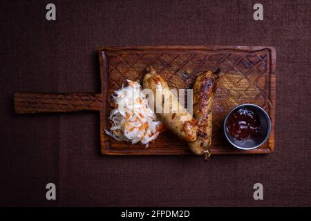 Gegrillte hausgemachte Würste mit Salzkohl auf dem Brett Stockfoto
