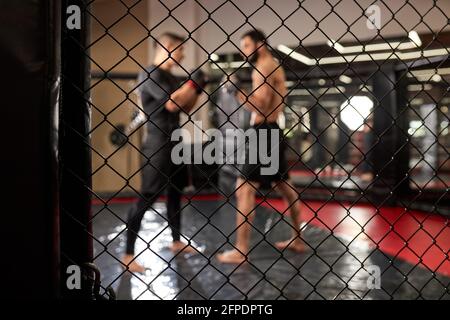 Zwei starke Männer Boxer Boxen, Ausübung thai Boxen in Silhouette, MMA. Blick durch den Käfig, im Ring im Fitnessstudio. Seitenansicht. Fokus auf Käfig, Nahaufnahme Stockfoto