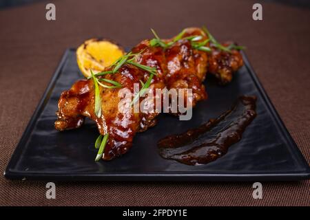 Gebackene Hähnchenflügel mit Sauce und Kräutern auf einem schwarzen Teller. Stockfoto