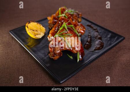 Gebackene Hähnchenflügel mit Sauce und Kräutern auf einem schwarzen Teller. Stockfoto