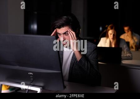 Beschäftigt ernster Mann Brainstorming, Denken über eine schwierige Frage, Blick auf den Computer, die Hände an Tempeln. Seitenansicht auf Brünette Kerl arbeiten Stockfoto